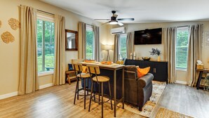 A modern living room with a dining area, wooden flooring, a ceiling fan, and large windows with curtains. - Hike & Fish: Nature Escape Near Licking River! (Cynthiana)
