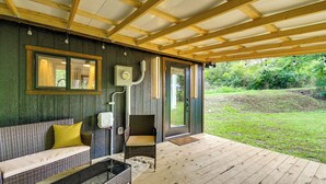 A covered porch with a wooden floor, a wicker sofa with a yellow cushion, a glass coffee table, and a wicker chair. - Hike & Fish: Nature Escape Near Licking River! (Cynthiana)