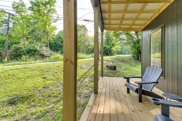 Una terraza de madera con sillas Adirondack y una mesa, con vistas a un césped con árboles.