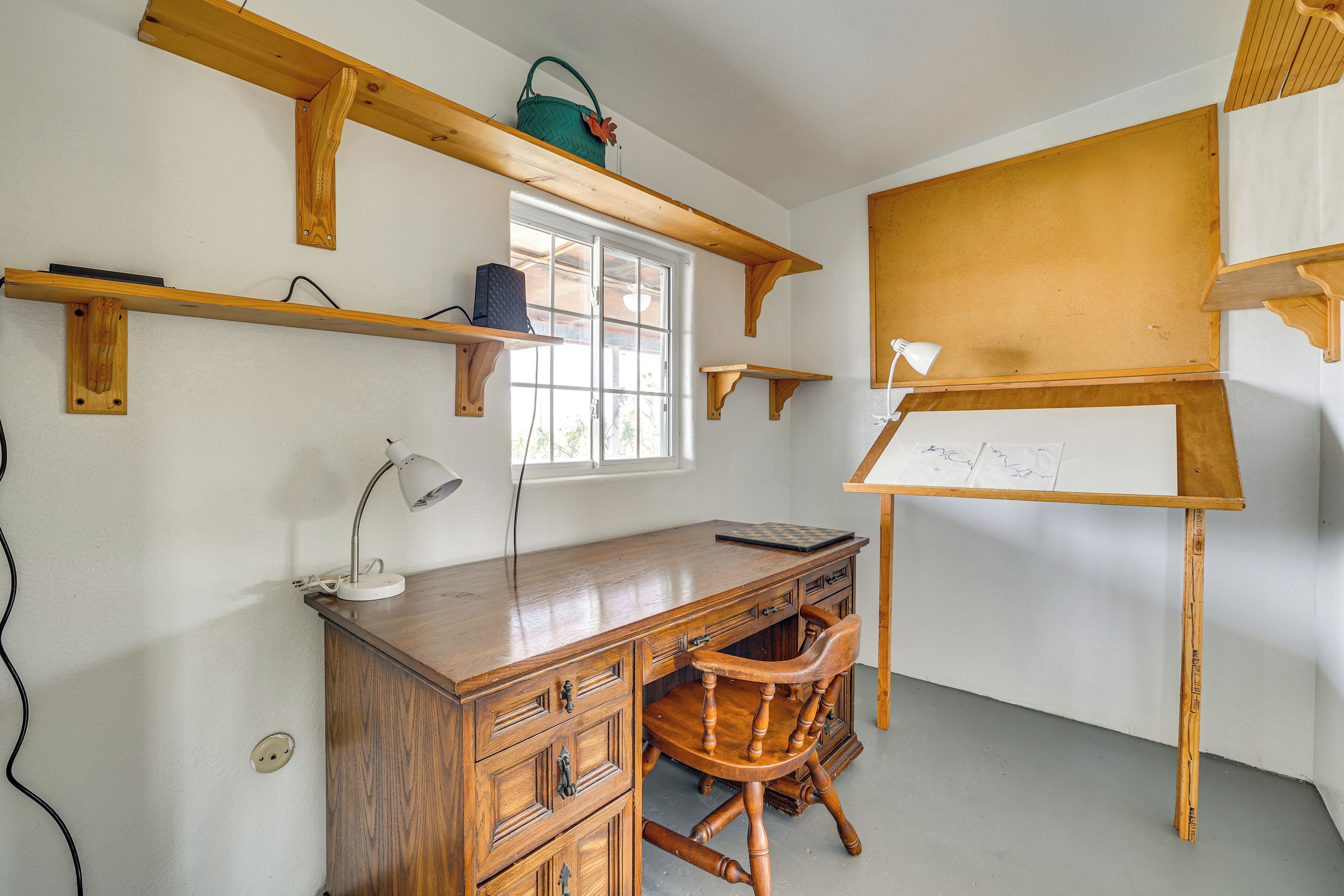Una habitació amb escriptori de fusta, una cadira, pissarra i prestatgeries amb diversos objectes.