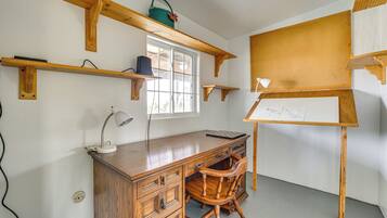 Una habitació amb escriptori de fusta, una cadira, pissarra i prestatgeries amb diversos objectes.