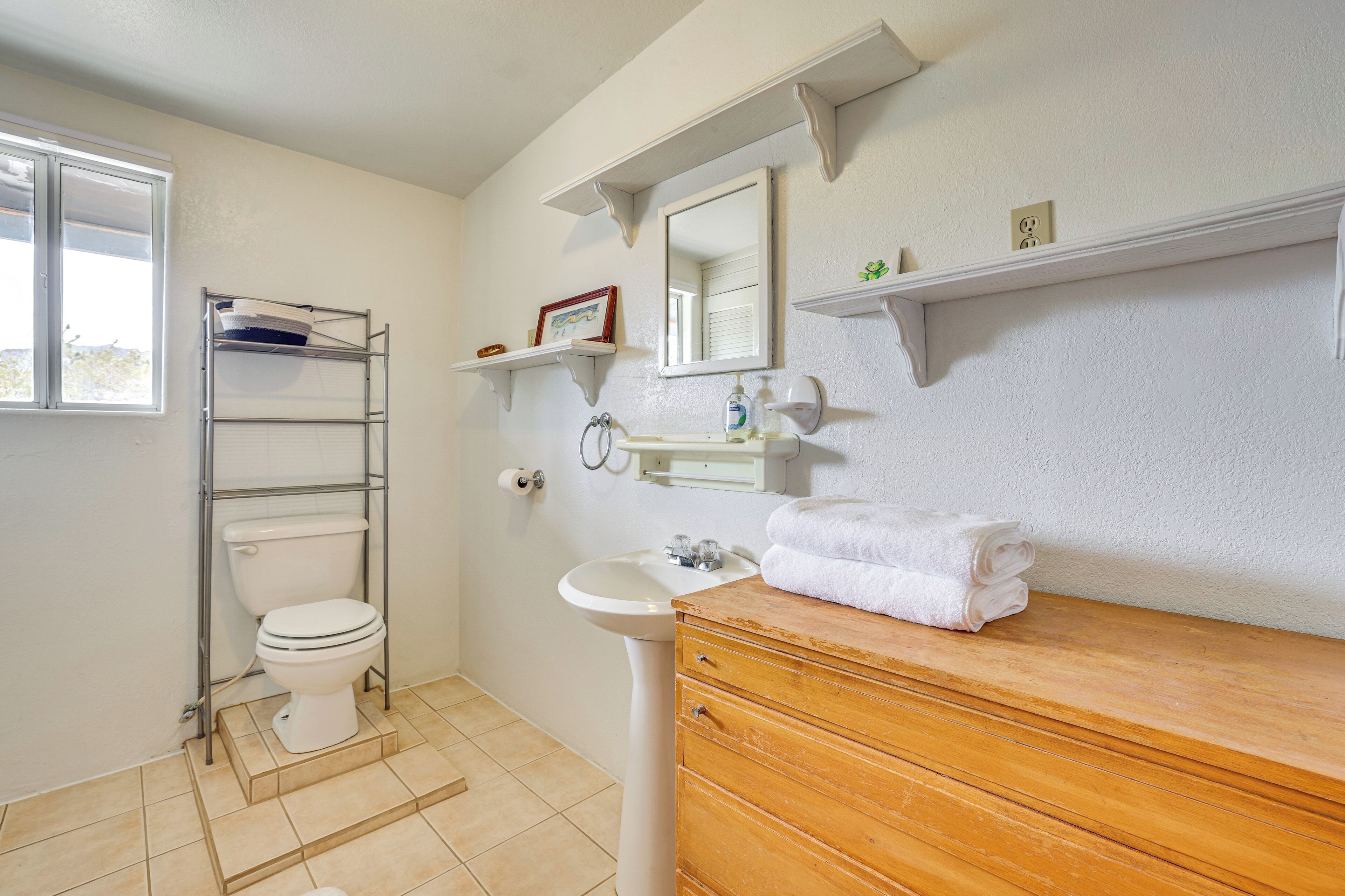 Une salle de bain comprenant des toilettes, un lavabo, un meuble-lavabo en bois et des étagères avec des articles de toilette.
