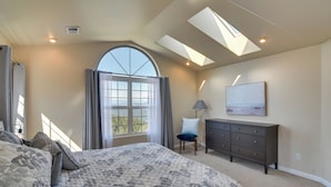 Une chambre à coucher avec un grand lit, une commode, une chaise, un puits de lumière et une fenêtre avec des rideaux.