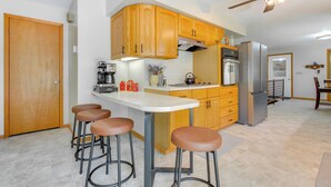 A kitchen with wooden cabinets, a white countertop, and a built-in stove. There are four stools and a ceiling fan. - 9 Mi to Downtown Rushville: Cozy Getaway w/ Grill (Rushville)