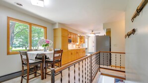 A kitchen with wooden cabinets, a dining table with chairs, and a view of trees through large windows. - 9 Mi to Downtown Rushville: Cozy Getaway w/ Grill (Rushville)