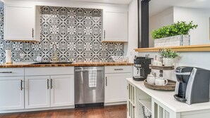 Ett modernt kök med vita skåp, en diskmaskin i rostfritt stål, ett mönstrat stänkskydd och en avdelning för kaffebryggning.