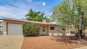 A single-story house with a garage, a small front yard with mulch, and a tree. - Pets Welcome: Hot Tub Haven in Albuquerque! (Albuquerque)