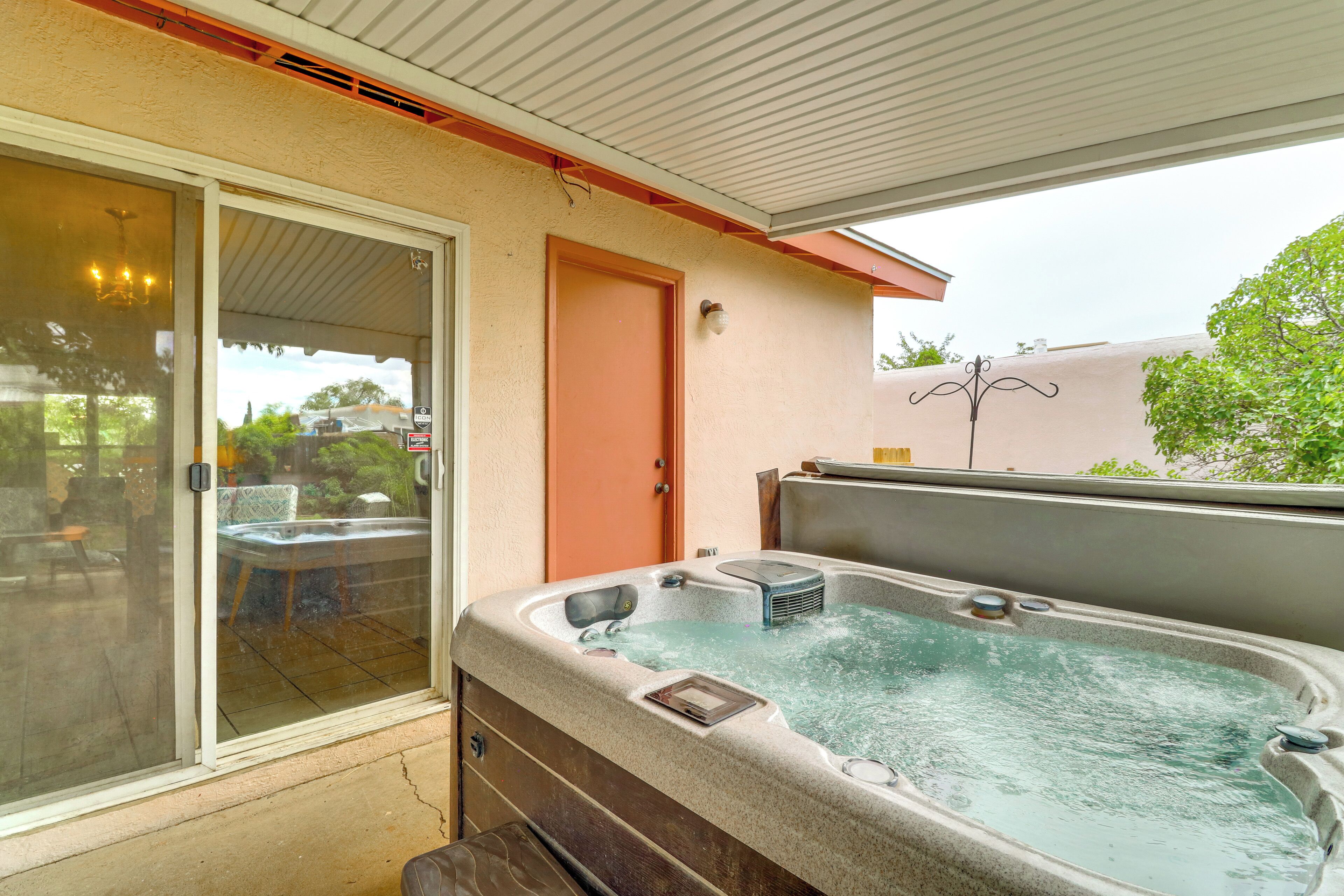 A hot tub on a covered patio with a sliding glass door leading to a backyard.