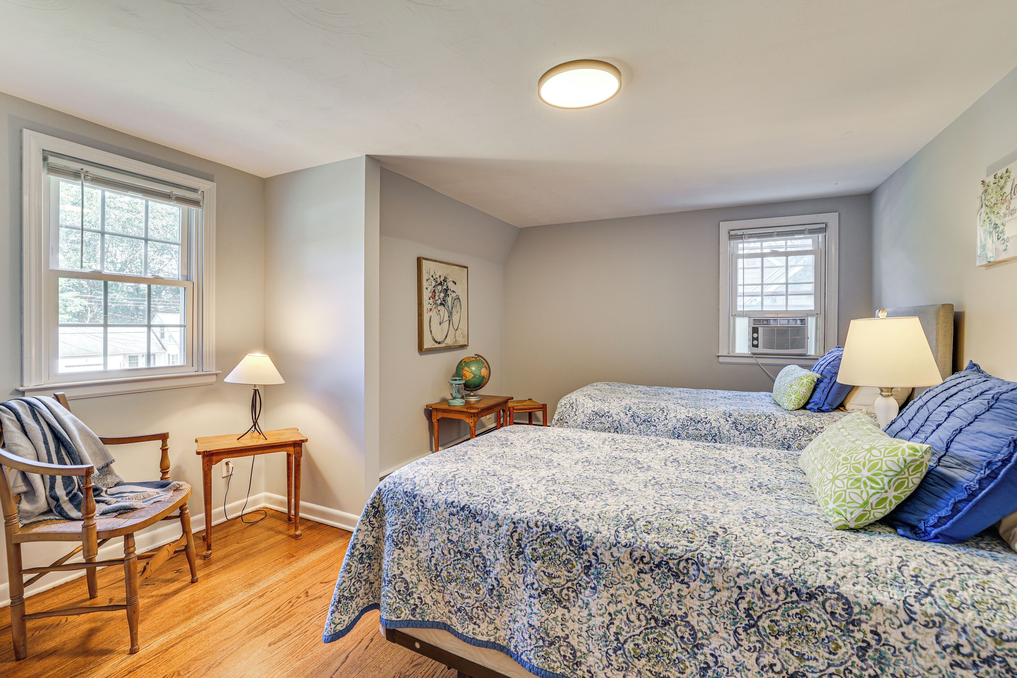 A bedroom with two beds, a chair, a table, and a globe on a nightstand.