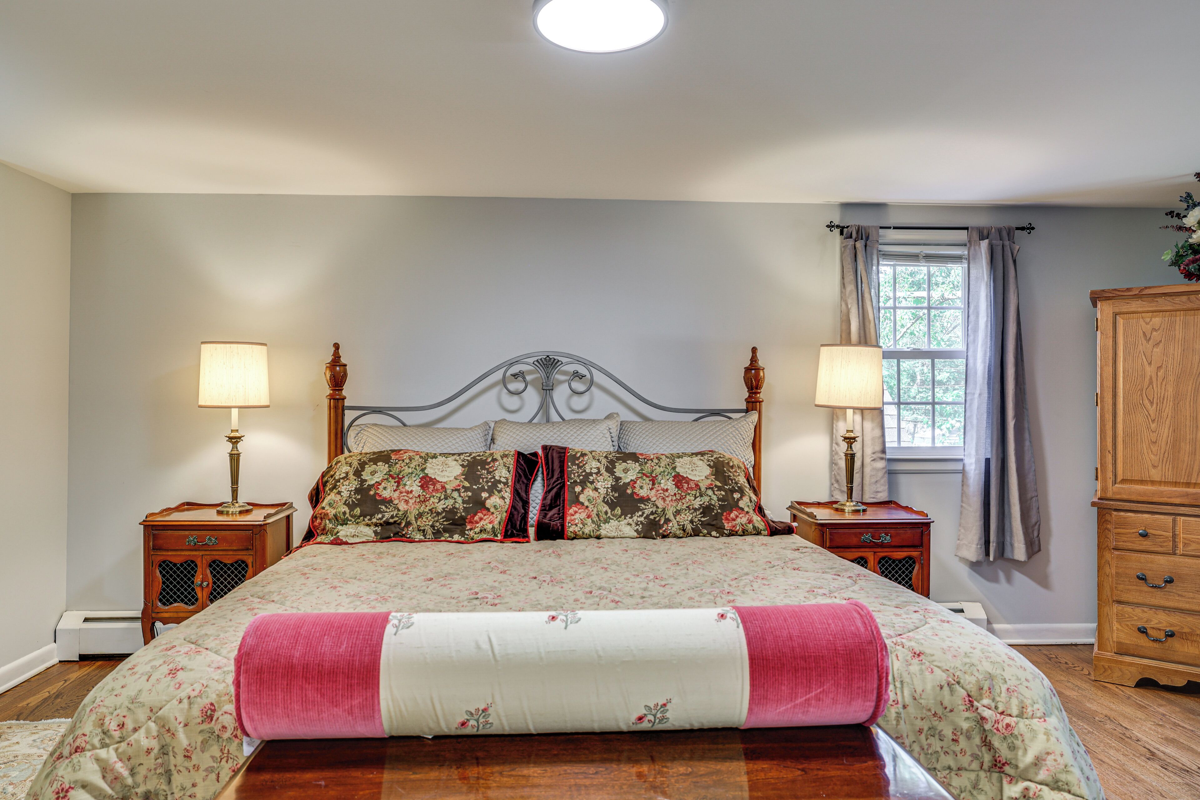 A bedroom with a large bed, two bedside tables, a wooden wardrobe, and a window with curtains.