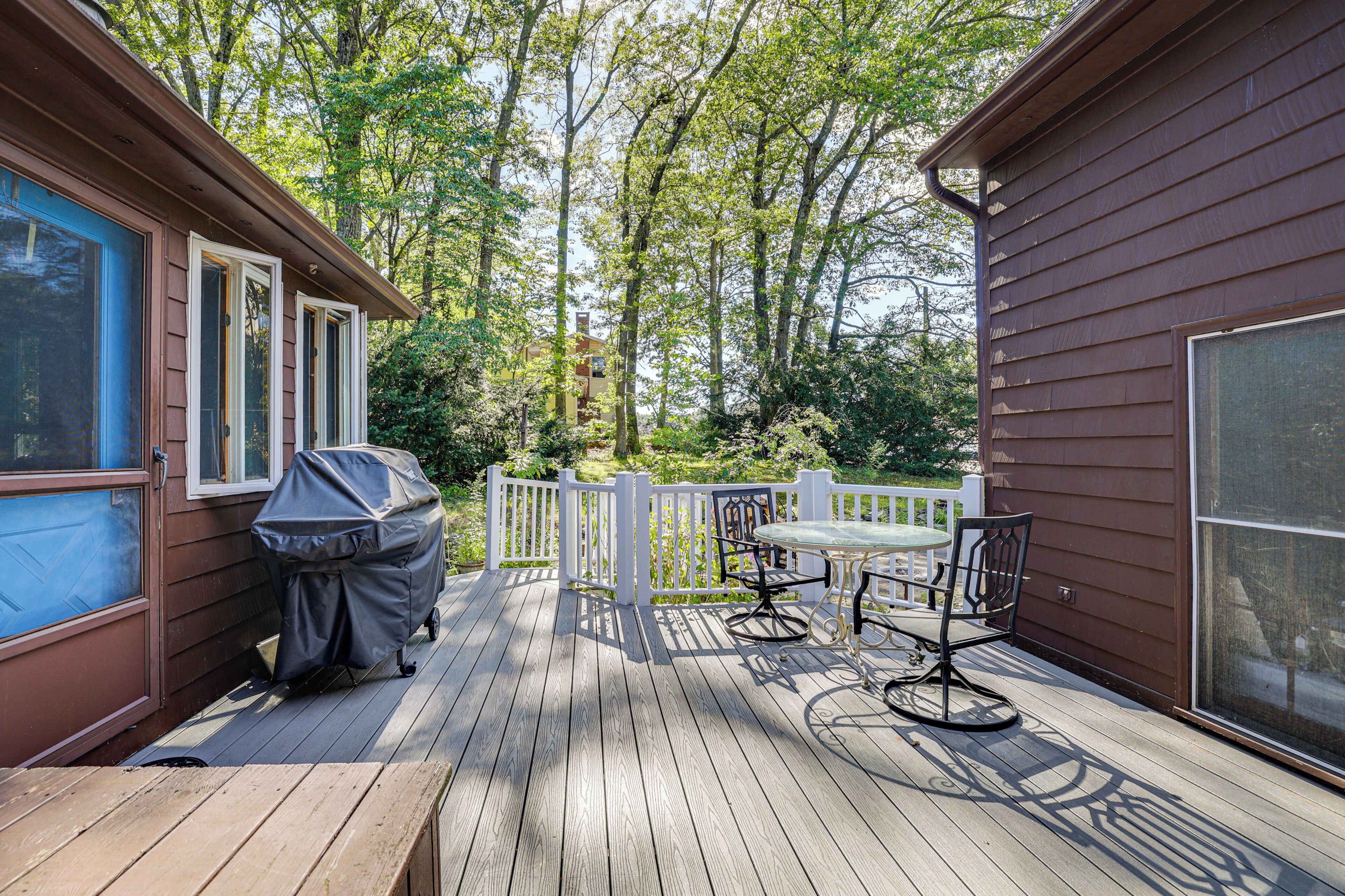 A wooden deck with a table and chairs, a barbecue grill, and a white fence.