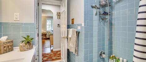 A bathroom with a shower, a sink, and a toilet. There is a towel rack and a bottle of shampoo on the sink.