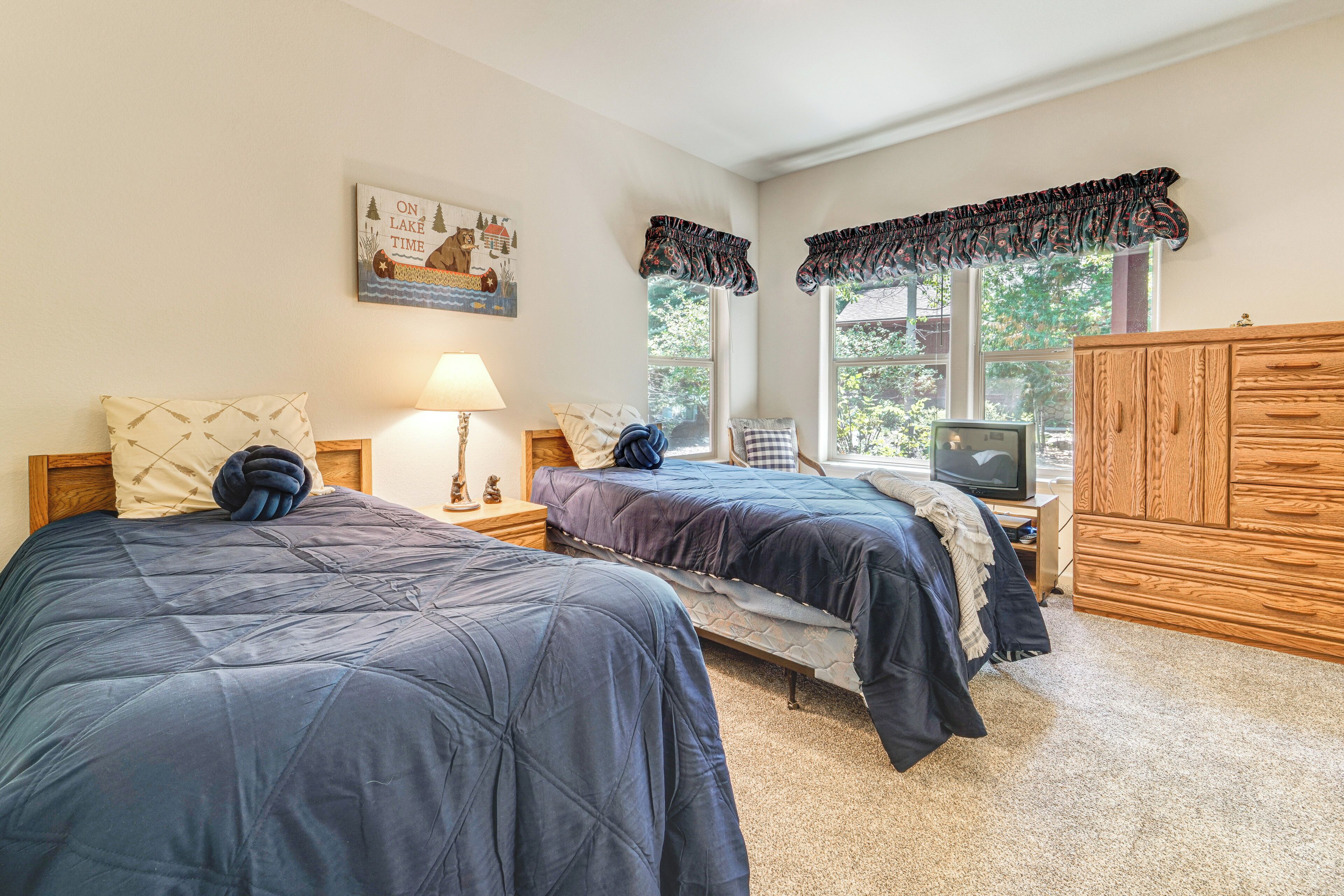 A bedroom with two beds, a wooden wardrobe, a television, and a window with curtains.