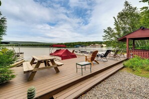A wooden deck with picnic tables and chairs, a covered area, and a view of a lake and hills. - Beech Mt Lakefront Gem! Hot Tub, Kayaks, Billiards (Drums)