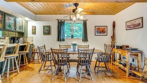 A dining area with a wooden table and chairs, a ceiling fan, and a window with curtains. - Beech Mt Lakefront Gem! Hot Tub, Kayaks, Billiards (Drums)