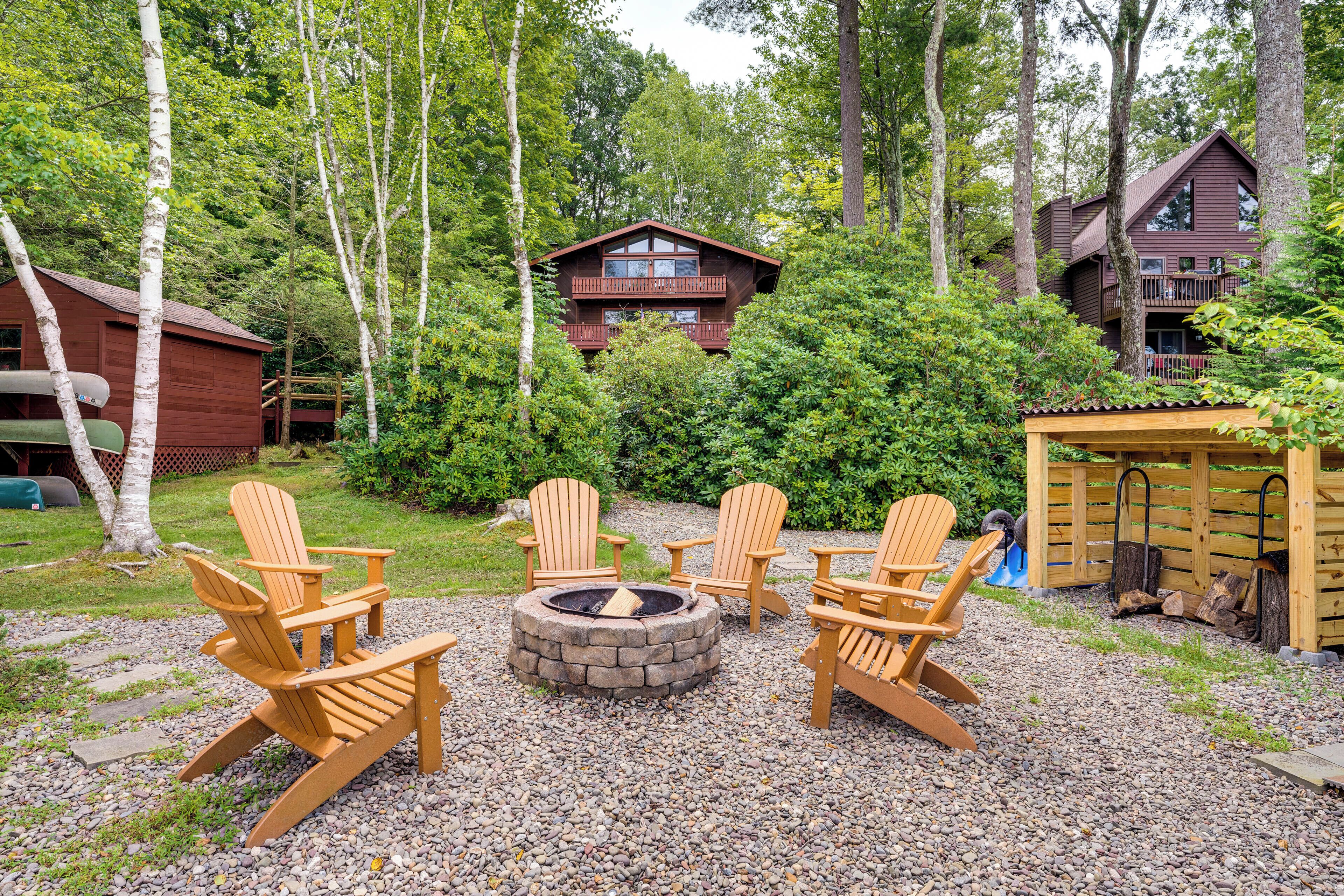 A cabin with a deck and a fire pit surrounded by Adirondack chairs.