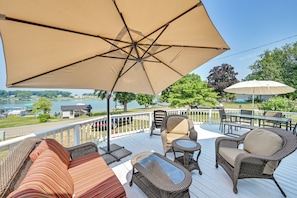 A deck with wicker furniture, a large umbrella, and a view of a lake.