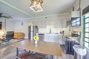 A modern kitchen with white cabinets, stainless steel appliances, and a wooden dining table with a vase of flowers. - 7 Mi to Dtwn Tulsa: Dog-friendly Home w/ Yard (Tulsa)