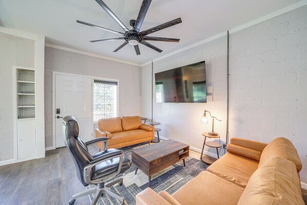 A living room with a sofa, a coffee table, a chair, a ceiling fan, and a TV mounted on the wall. - 7 Mi to Dtwn Tulsa: Dog-friendly Home w/ Yard (Tulsa)
