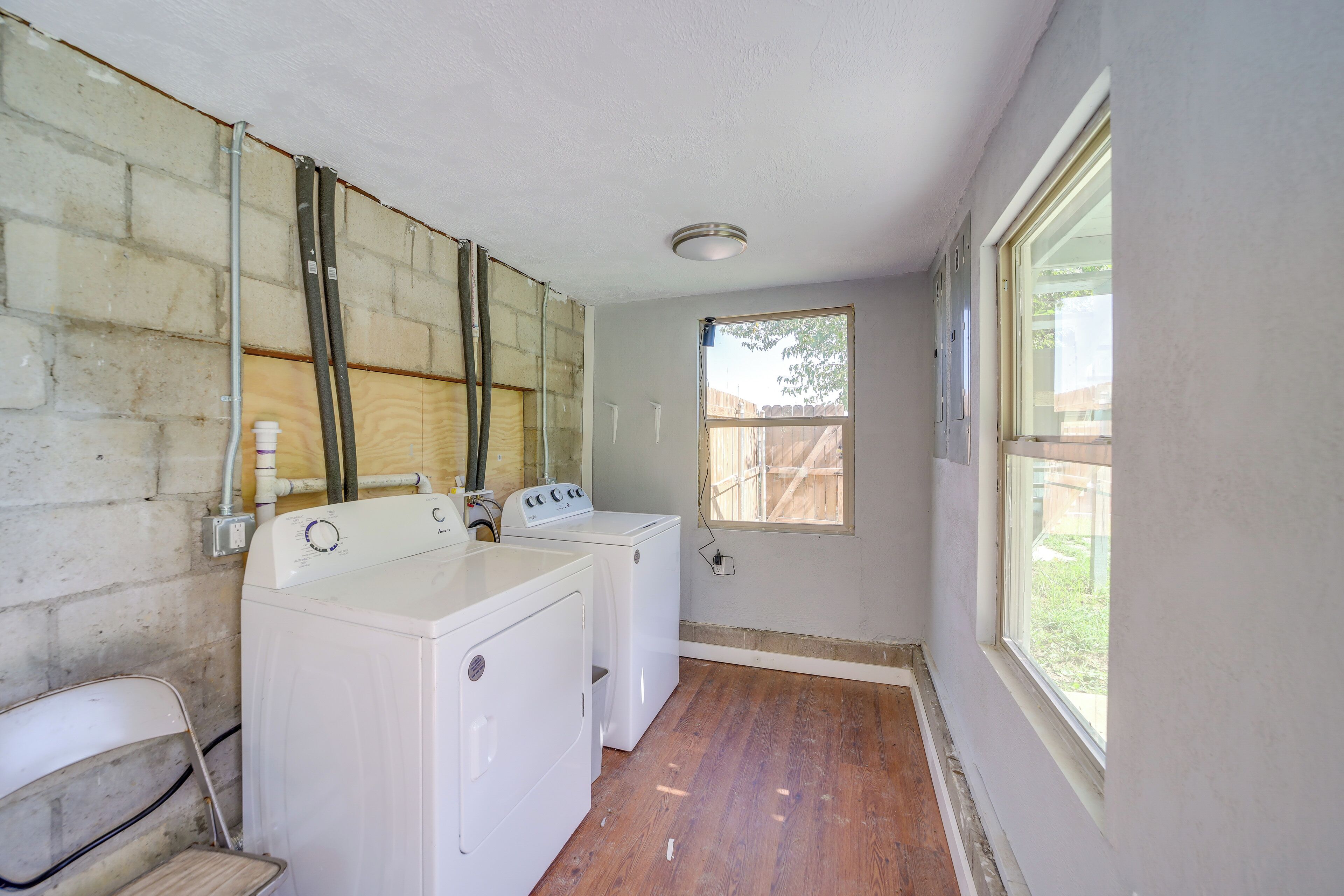 Une buanderie avec deux machines à laver blanches, un plancher en bois et une fenêtre donnant sur une clôture en bois.