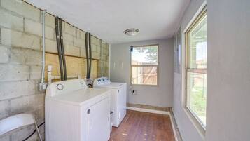 A laundry room with two white washing machines, a wooden floor, and a window with a view of a wooden fence.