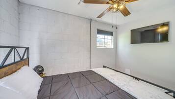 A bedroom with a bed, a ceiling fan, a window, and a TV mounted on the wall.