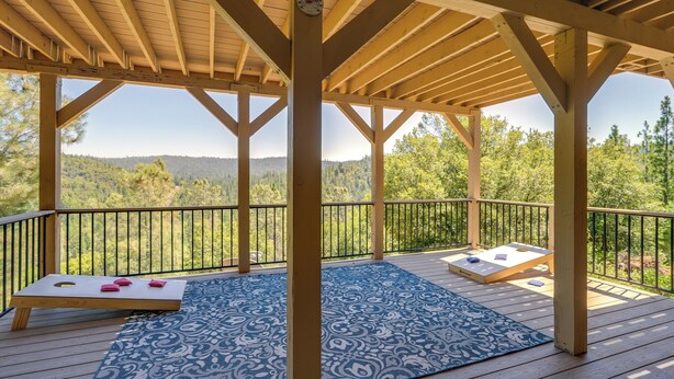 Una terraza de madera con un tapete azul estampado, dos bancos de madera y una pérgola de madera con un reloj.