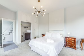 A bedroom with a large bed, a dresser, a nightstand, a ceiling light fixture, and a staircase leading to another room. - Game Days, Grubs & More: Updated Cincinnati Home! (Cincinnati)