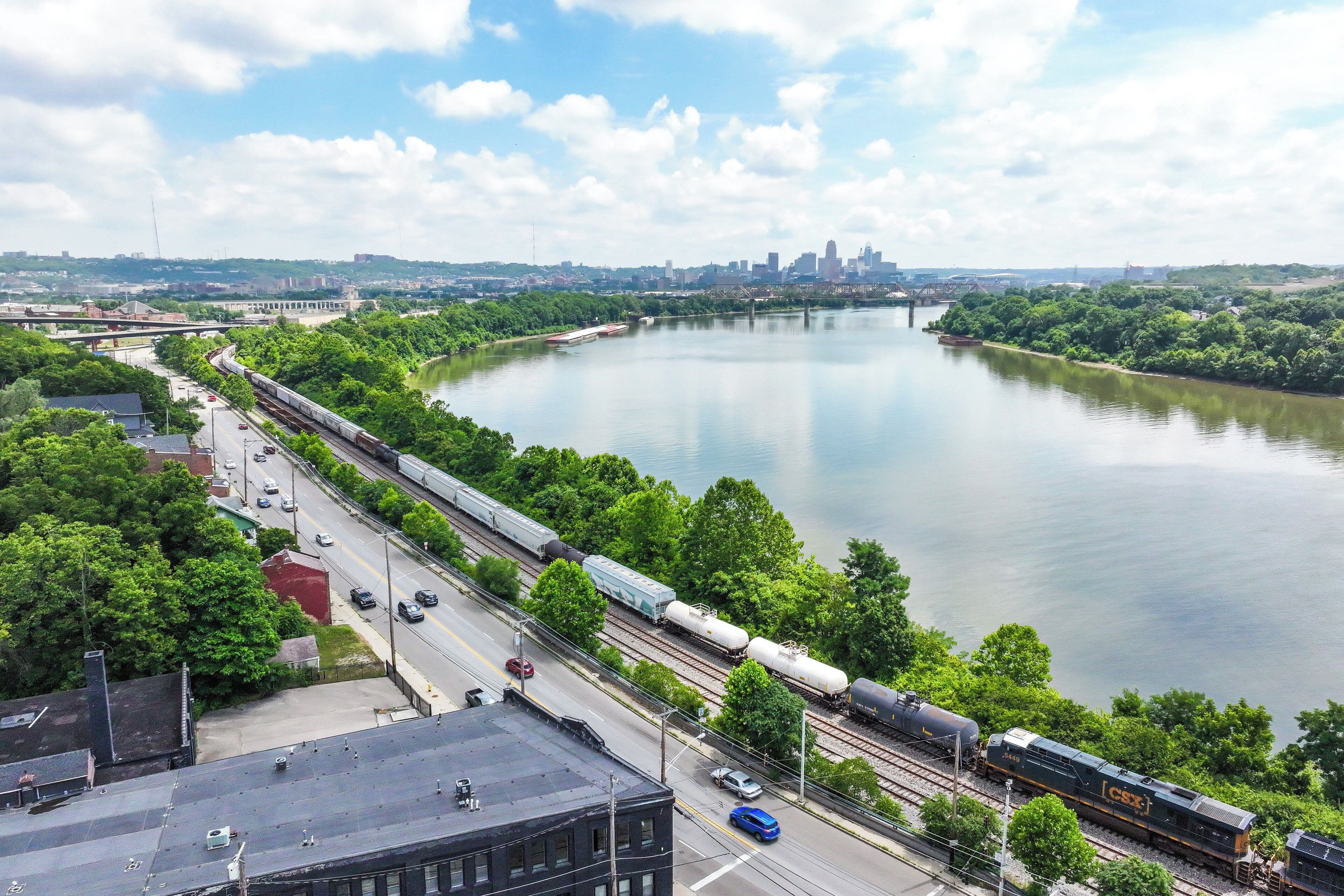 A train passing by a river with a city skyline in the background.