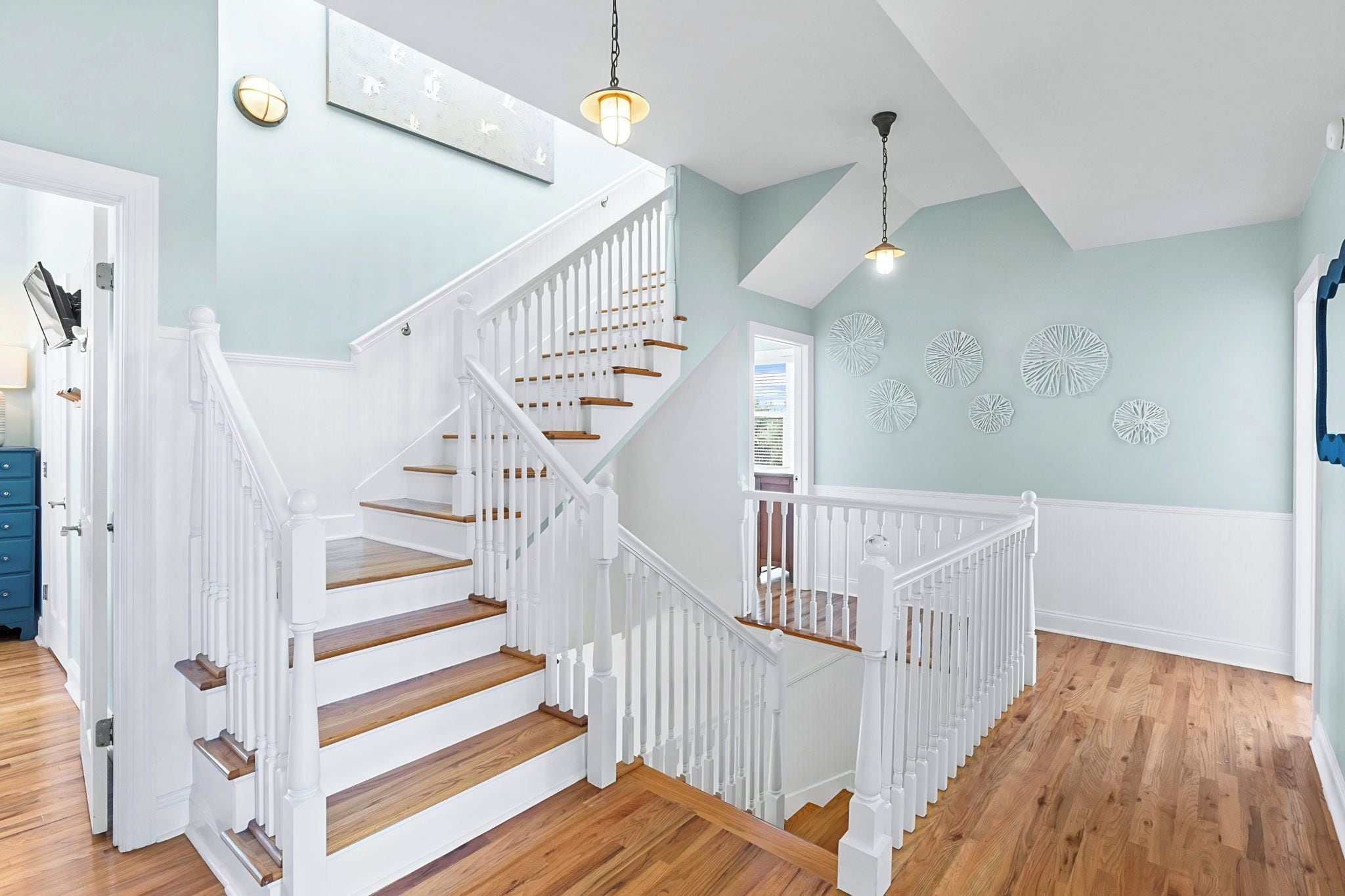 A staircase with white railings and wooden steps, leading to a landing with a light blue wall and decorative wall art.
