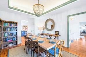 A dining area with a wooden table set for four, surrounded by chairs. There is a bookshelf to the left and a mirror on the wall above the table. - Private Pool & Hot Tub, 360° Porch, Steps to Beach (Port St. Joe)