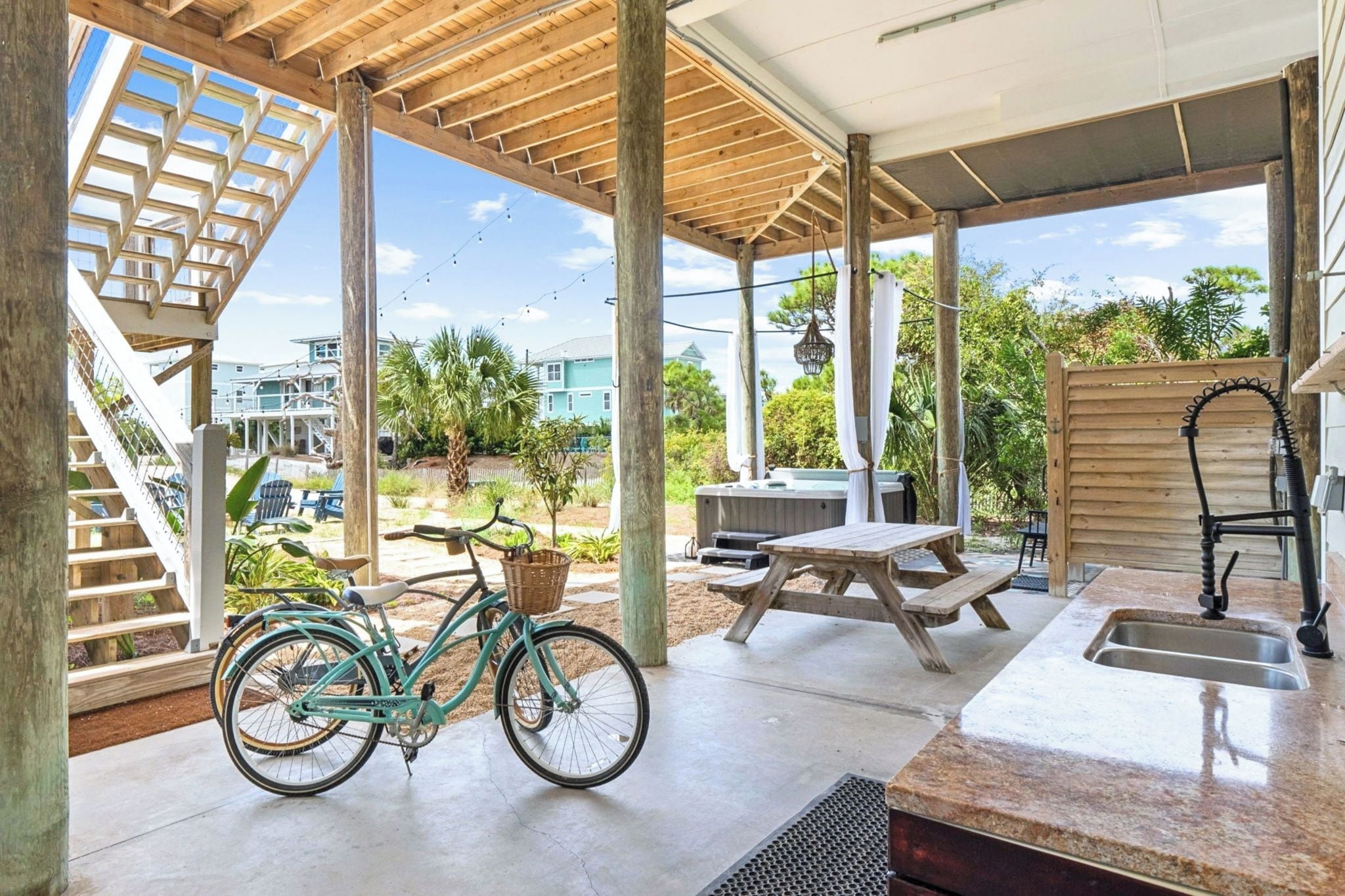A covered outdoor area with a wooden bench, a picnic table, a bicycle, and a hot tub.