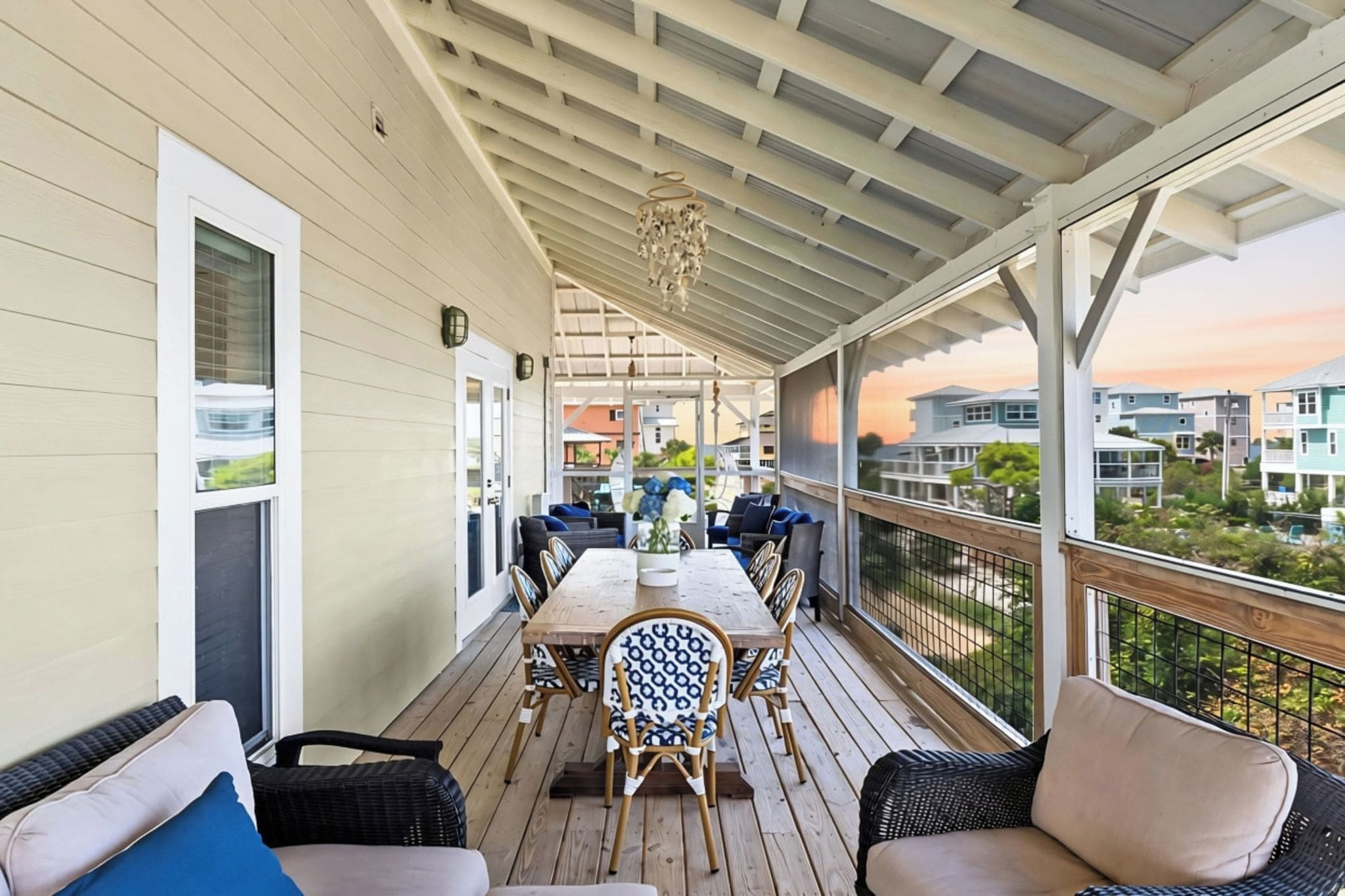 A covered outdoor area with a dining table and chairs, a railing, and a view of the surrounding neighborhood.