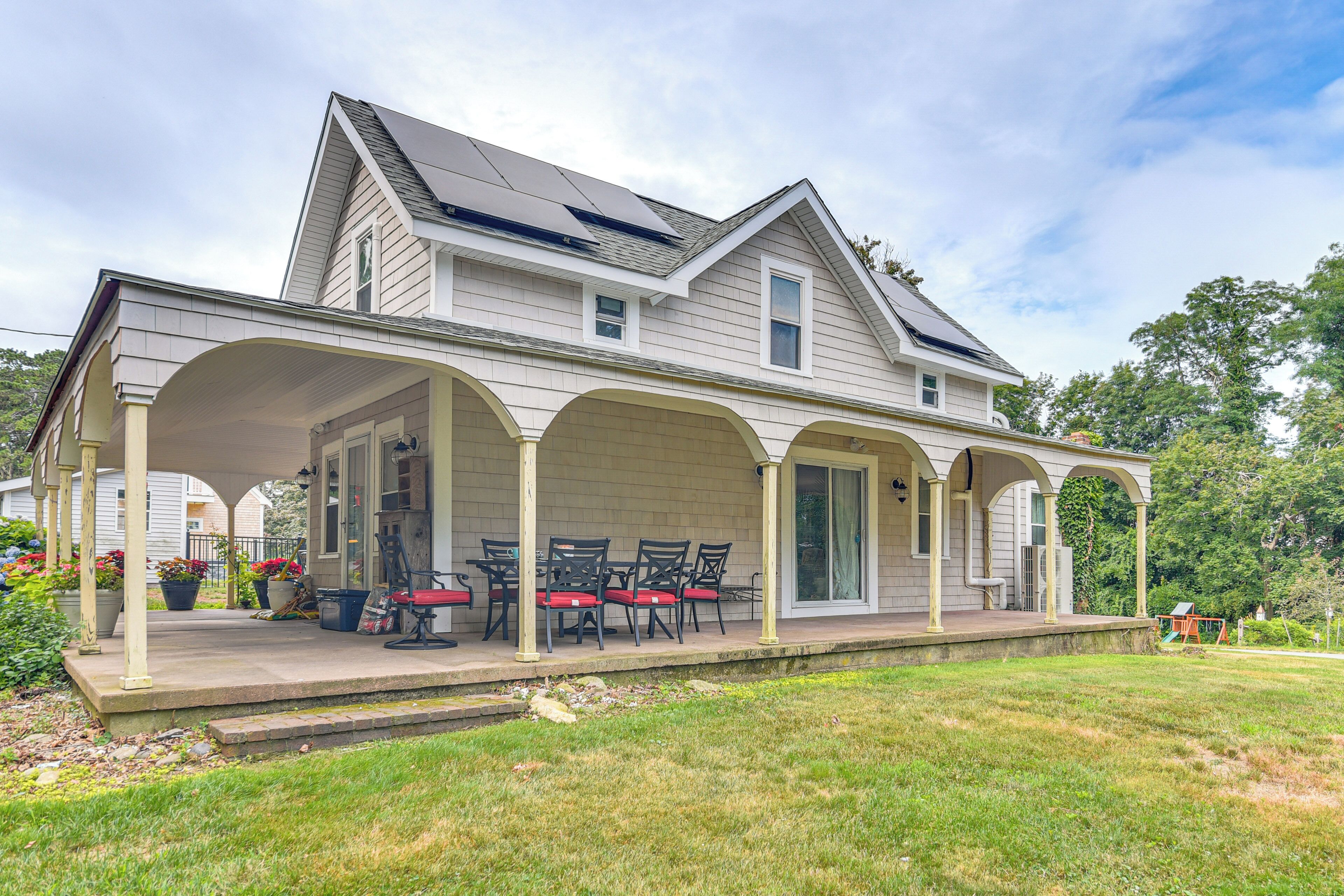 A two-story house with a covered porch, a dining area with chairs, and a small play area in the yard.