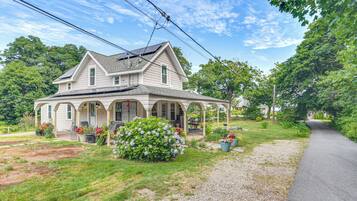 A two-story house with a covered porch, a garden with potted plants, and a gravel driveway.