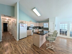 Una cocina con suelo de madera, una isla central y una zona de comedor con una silla.