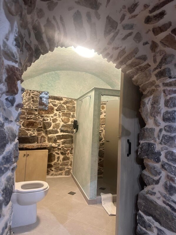 A stone-walled bathroom with a toilet, a sink, and a shower area.