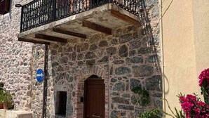 Un bâtiment en pierre avec une porte en bois, un balcon orné de balustrades en fer forgé et des plantes en pot.
