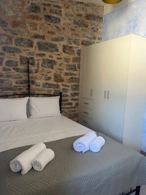 Un dormitorio con pared de piedra, cama con ropa blanca, armario y toallas enrolladas sobre la cama.