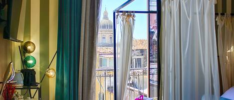 A hotel room with a bed, a desk with a lamp, and a view of a building with a dome.