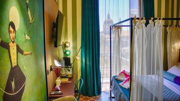 Habitación de hotel con cama, escritorio con lámpara, silla y vista a un edificio a través de una ventana.