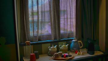 Una ventana con cortinas, una mesa con teteras, tazas y un hervidor.