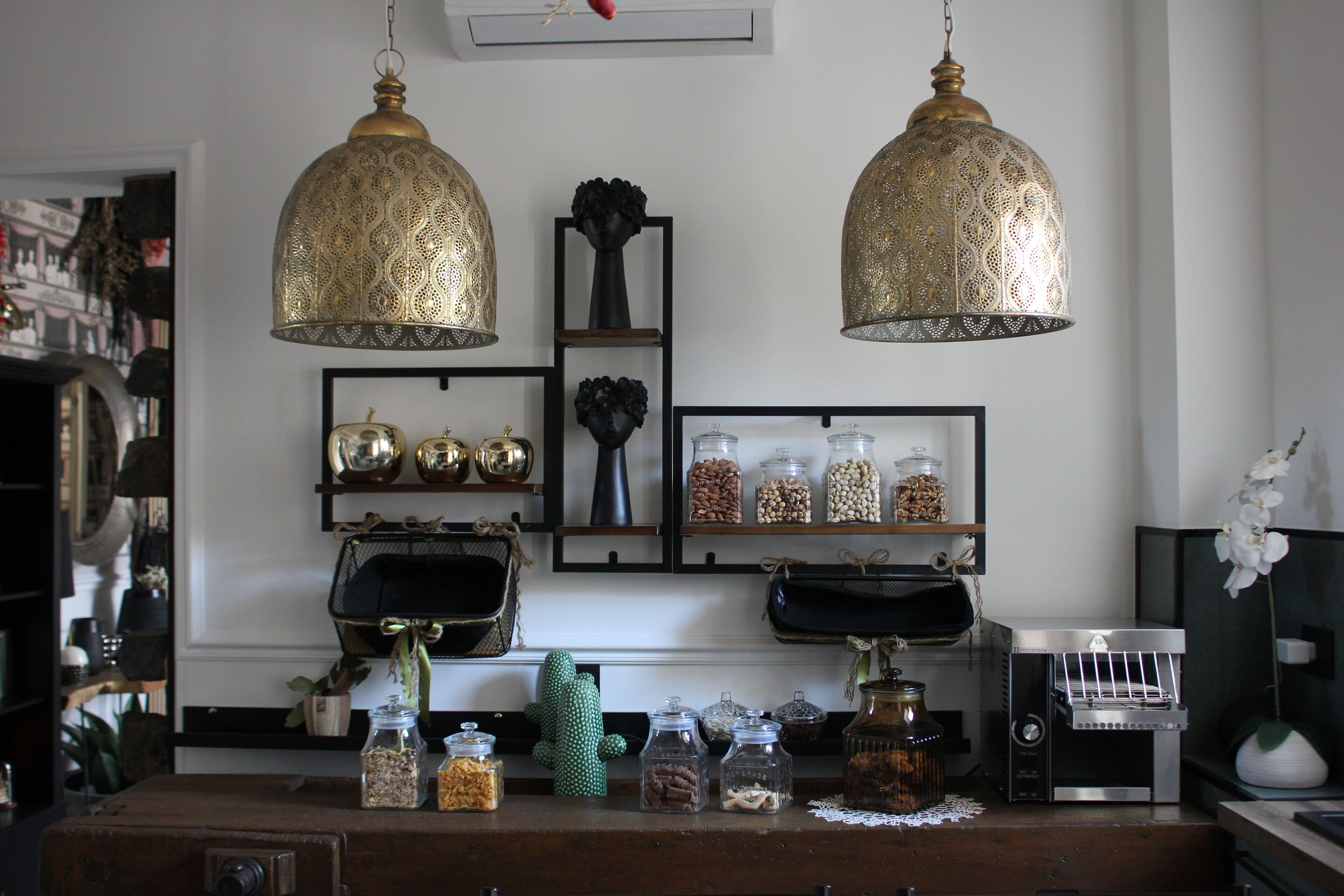Cozinha com duas luminárias pendentes, prateleiras com potes e uma máquina de café.