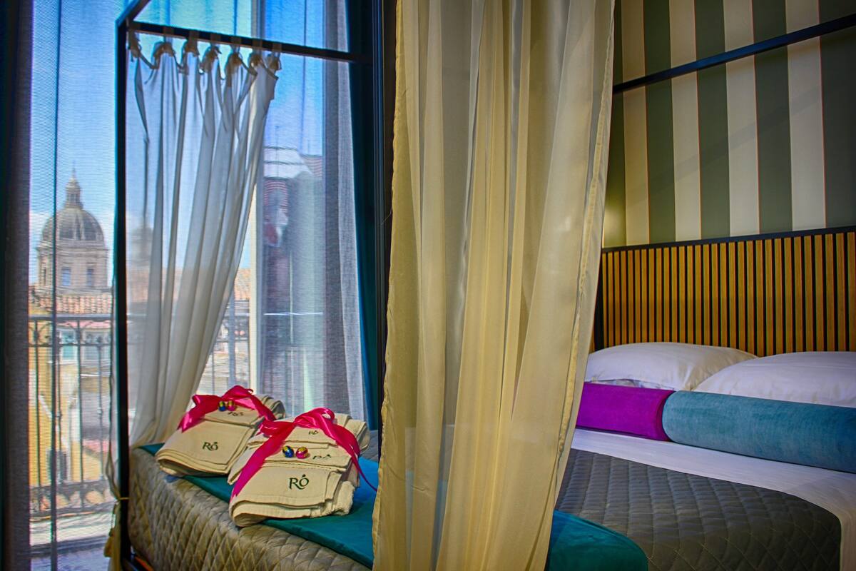 A hotel room with a bed, a window with curtains, and a view of a building outside.