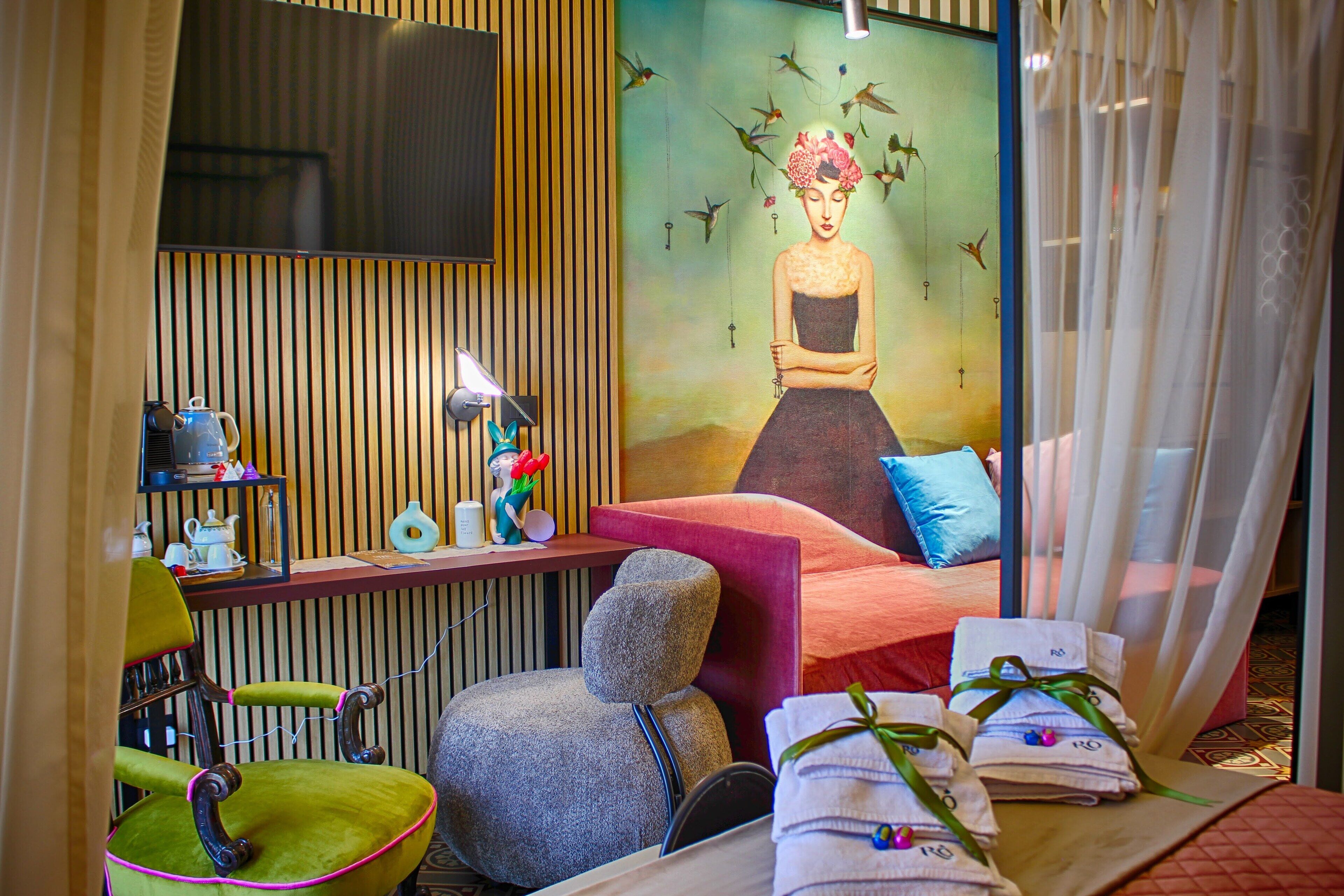 A room with a bed, a chair, a desk, and a wall painting.