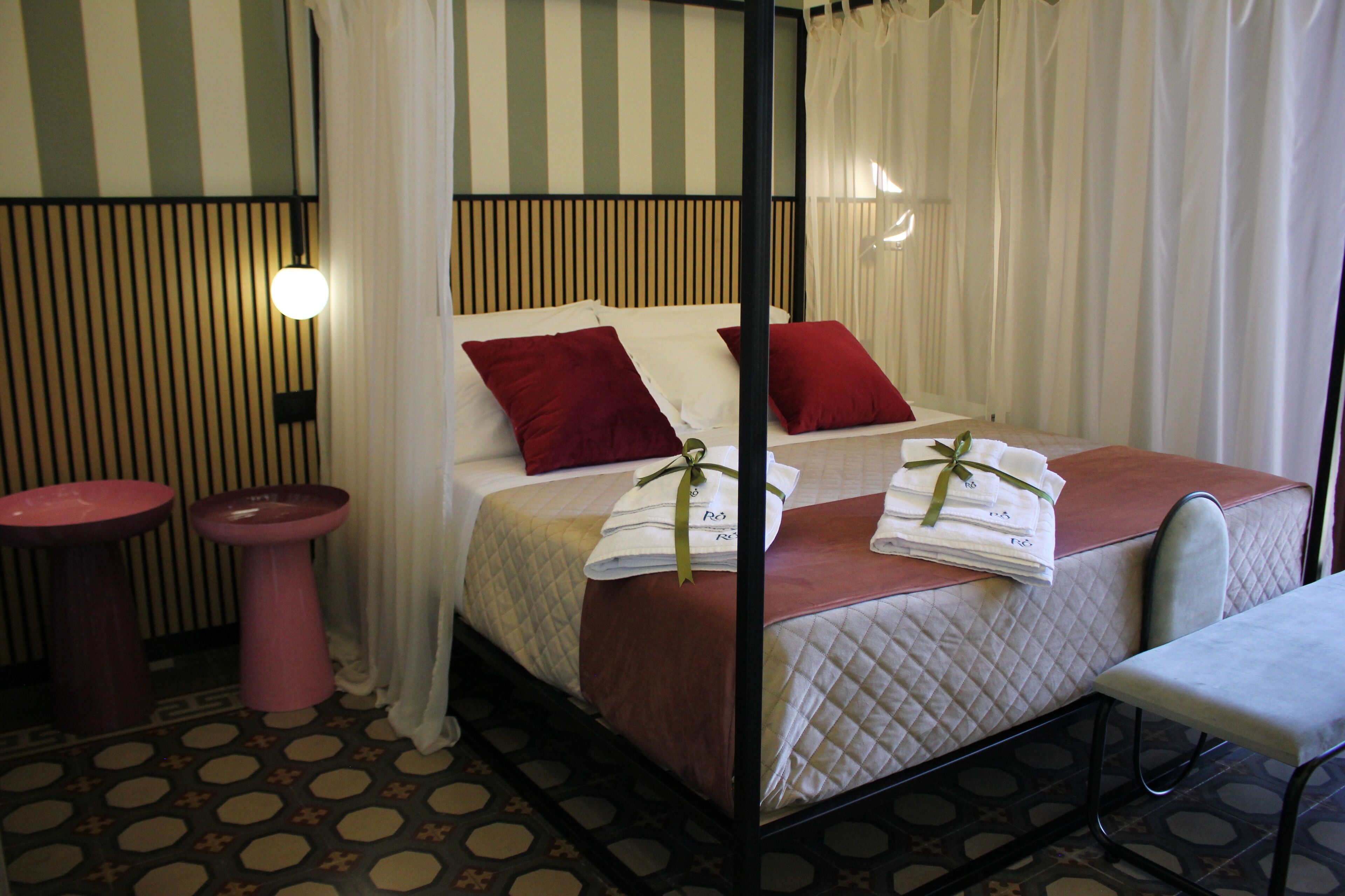 Une chambre d’hôtel avec un lit, une table de chevet, une chaise et un petit tabouret.