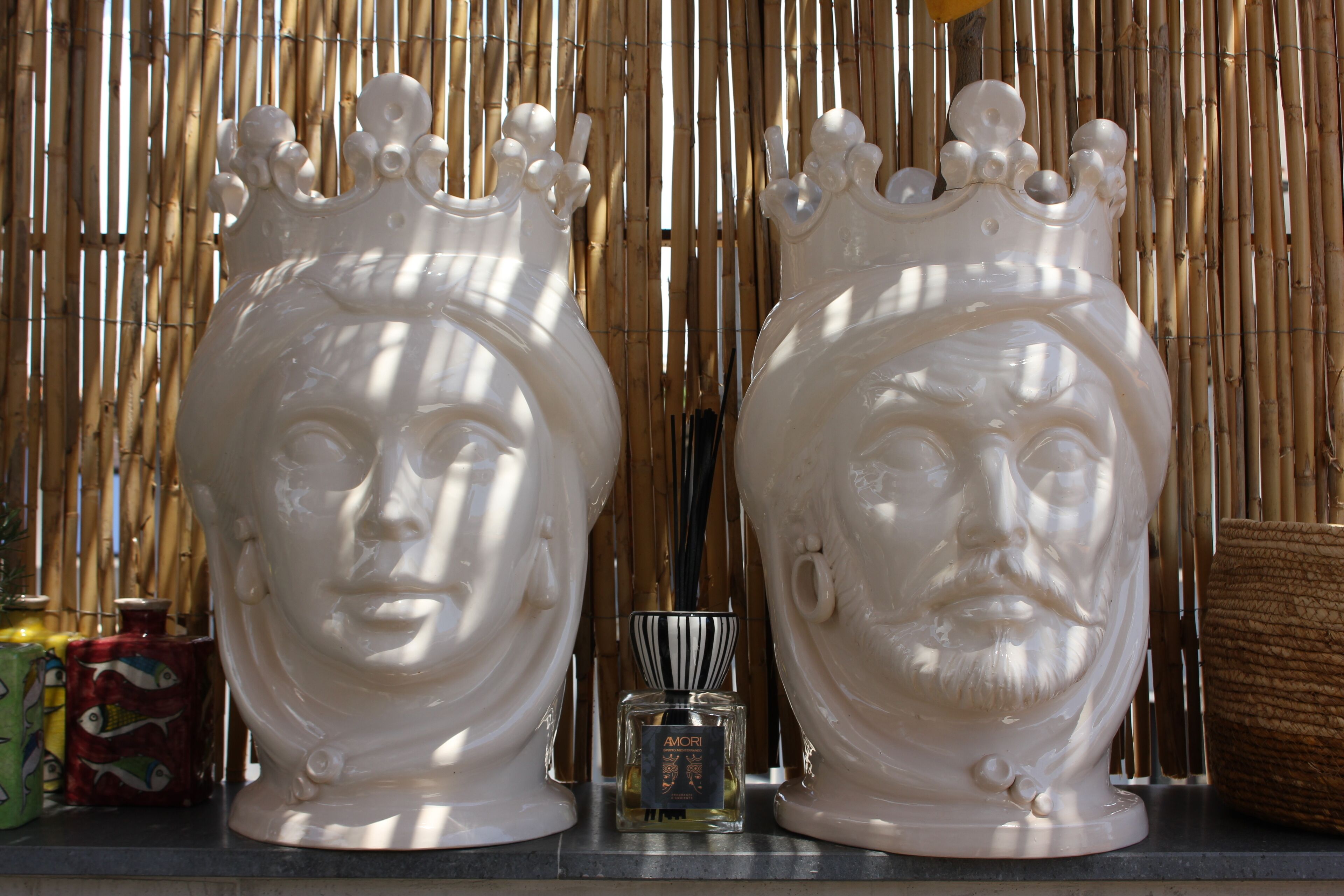 Two white decorative vases with a crown design, placed on a shelf with a bamboo backdrop.