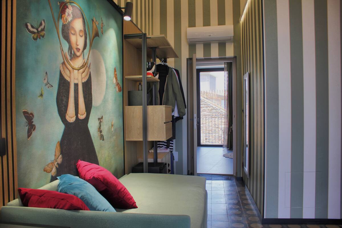 A hotel room with a bed, pillows, a wardrobe, a mirror, and a wall with a butterfly mural.