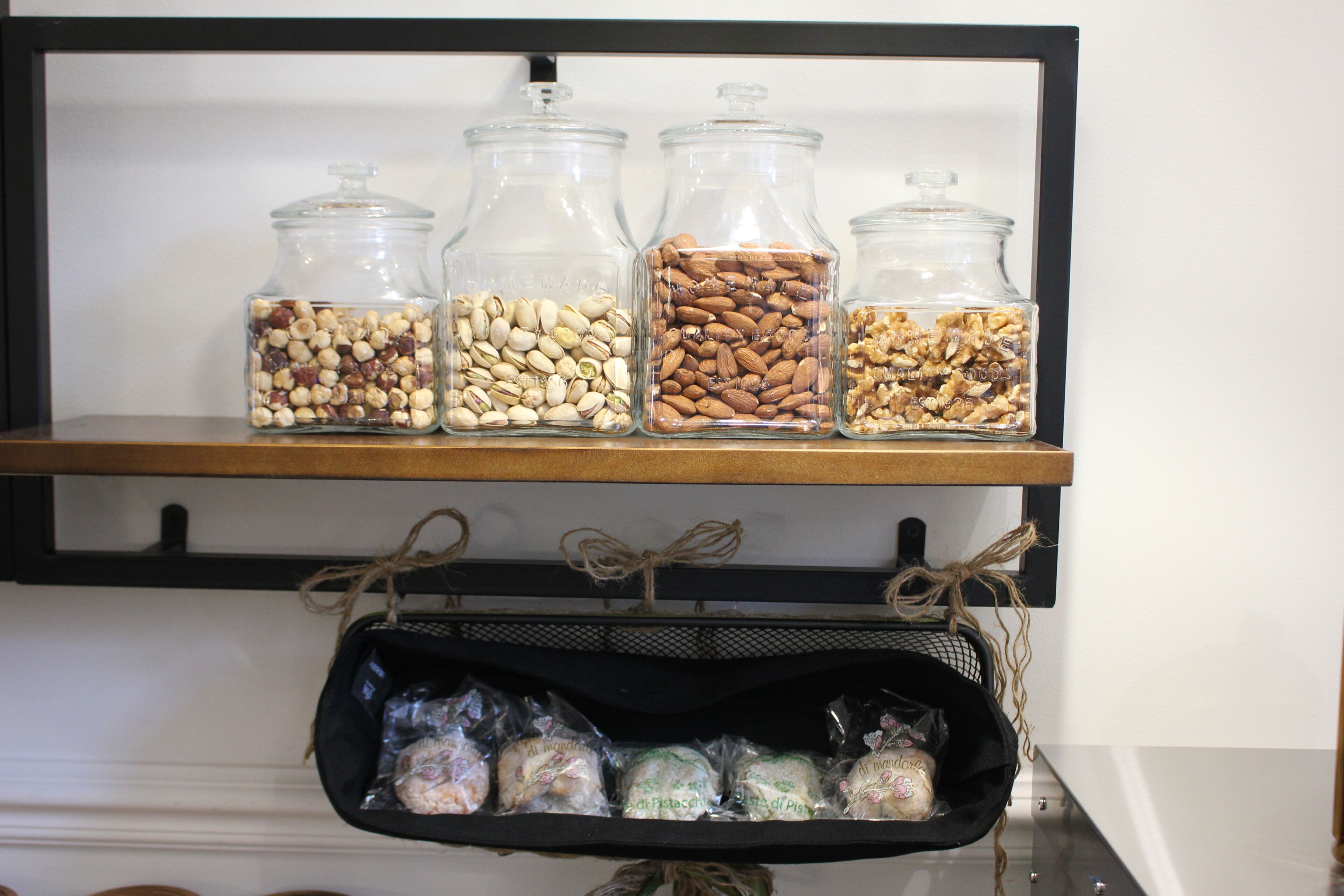 A shelf with glass jars containing nuts and a basket with packaged food items.