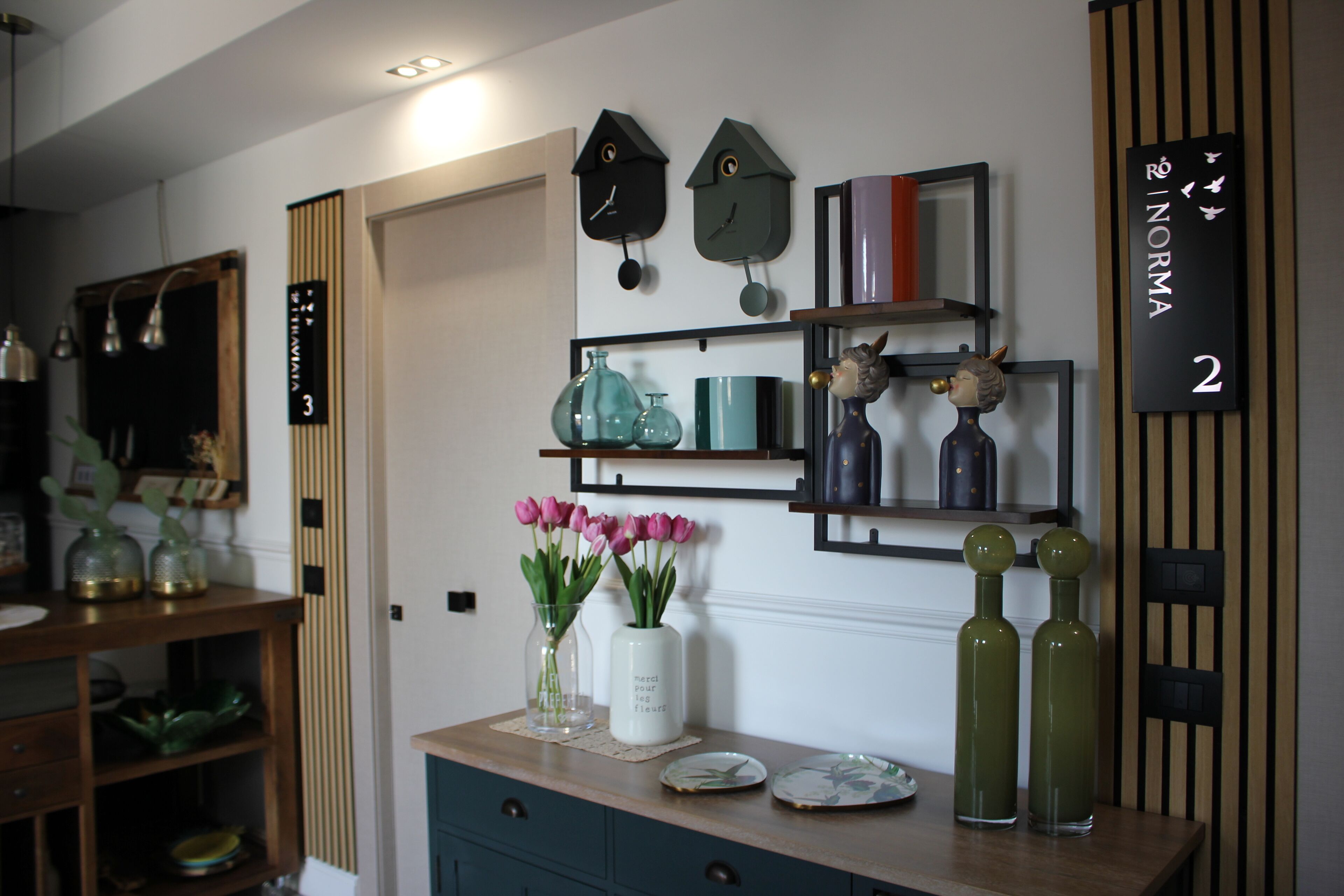 A room with a wooden door labeled '3', a wall-mounted clock, a shelf with decorative items, and a vase with pink flowers.